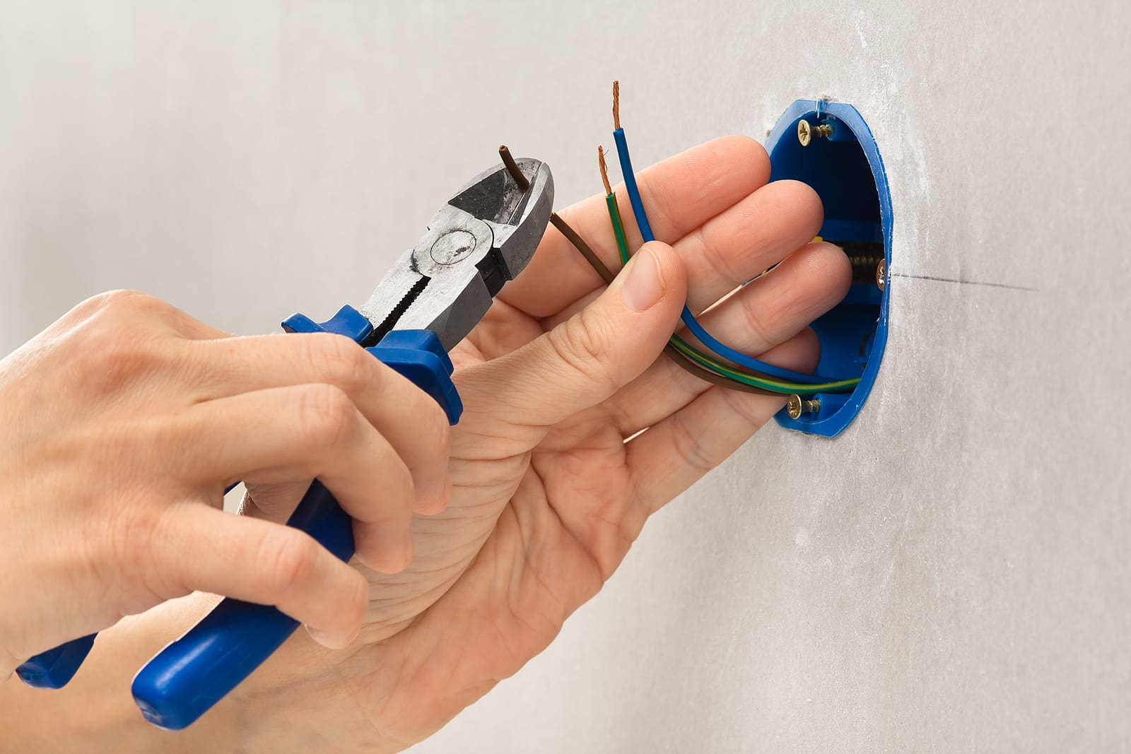 TNS Electric A person uses wire cutters to trim electrical wires extending from a blue wall-mounted electrical box.
